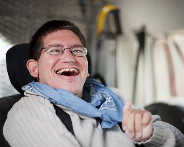 Ein junger Mann mit Behinderung sitzt in einem Fahrzeug und lacht | © Caritas München und Oberbayern