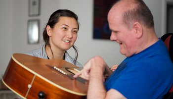 Behindertenpflegerin und behinderter Patient beim Gitarre spielen | © Gary Radler/Getty Images iStockphoto